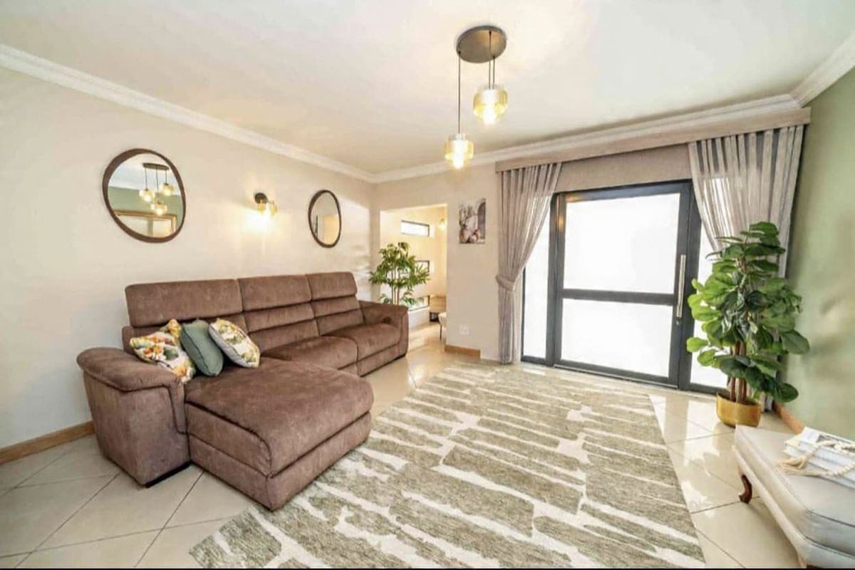 A well-maintained living room featuring tiled flooring, modern pendant lighting, and a large sliding glass door providing natural light.