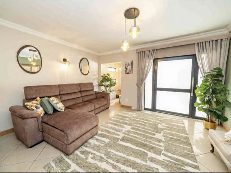 A well-maintained living room featuring tiled flooring, modern pendant lighting, and a large sliding glass door providing natural light.