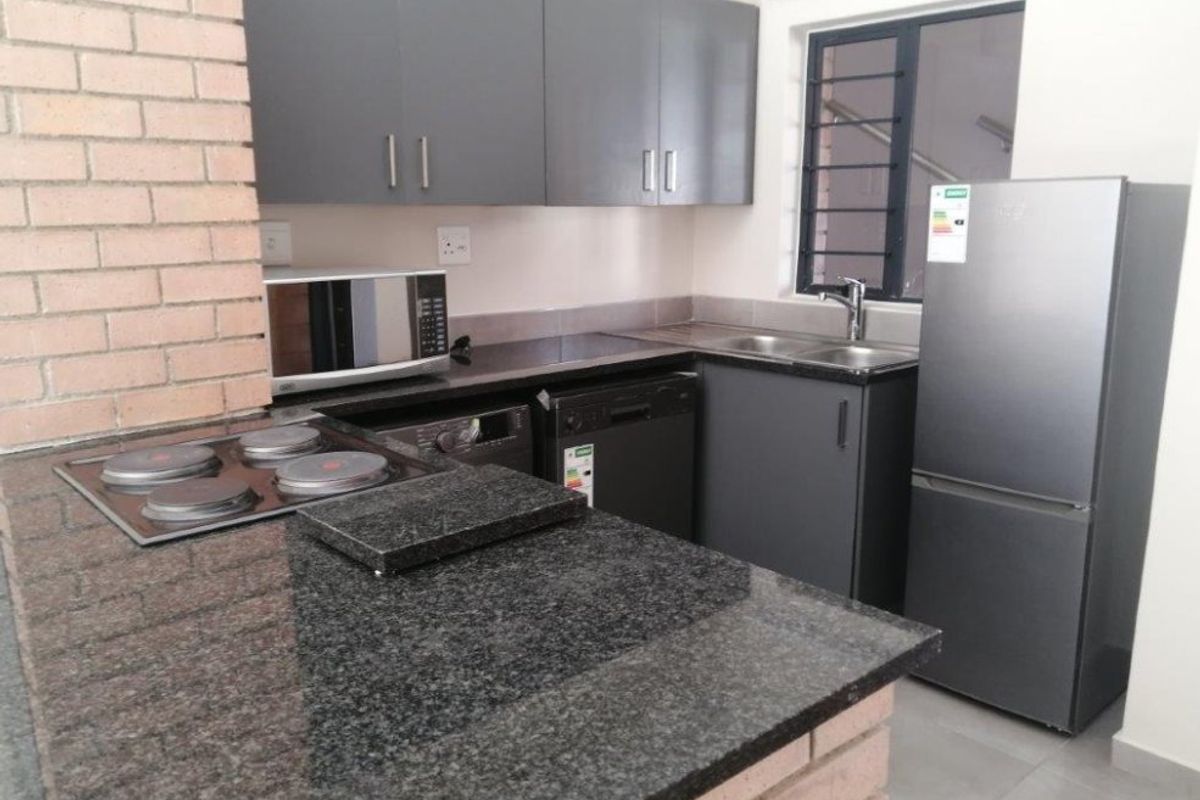 Modern kitchen featuring dark grey cabinetry, granite countertops, a built-in hob, and a distinctive brick feature wall.