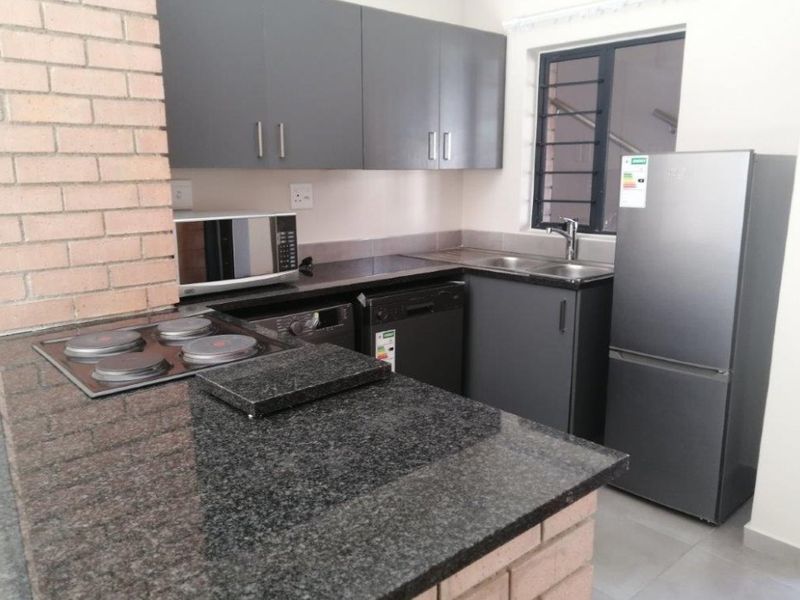 Modern kitchen featuring dark grey cabinetry, granite countertops, a built-in hob, and a distinctive brick feature wall.