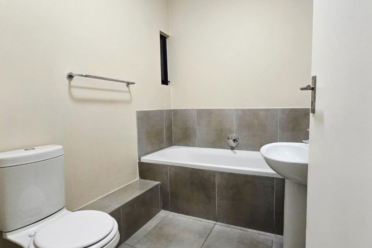 A clean, modern bathroom featuring a built-in bathtub with tiled surround, a pedestal washbasin, and a standard toilet.