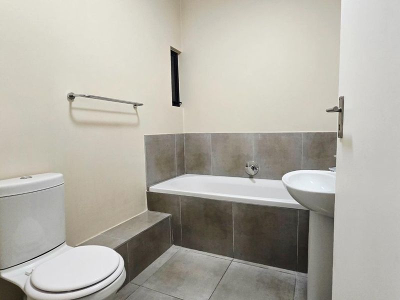 A clean, modern bathroom featuring a built-in bathtub with tiled surround, a pedestal washbasin, and a standard toilet.