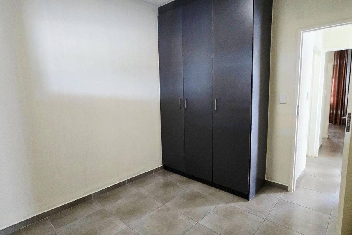 A clean, empty bedroom featuring modern dark built-in cupboards and neutral tiled flooring, offering a versatile space ready for personalization.