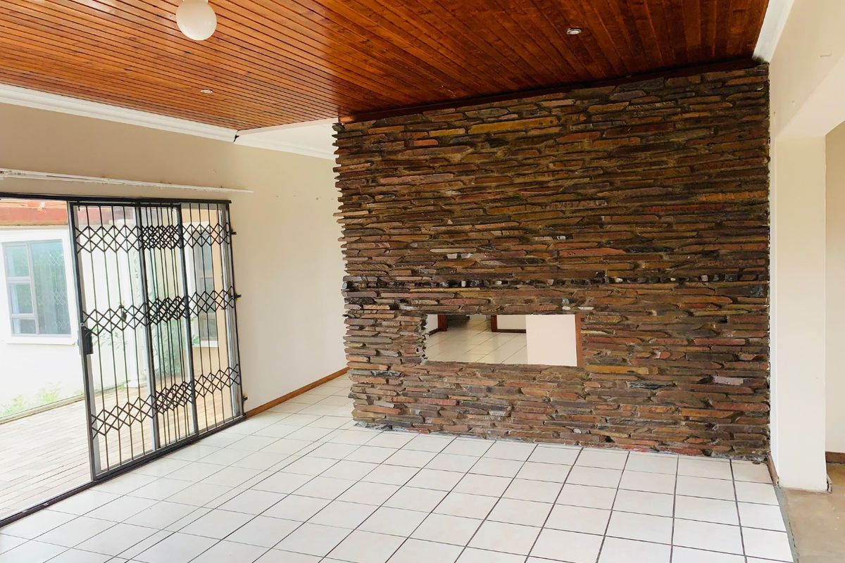 Spacious living area featuring a prominent stone fireplace wall, timber ceiling, and large sliding glass doors with security gates leading to the exterior.