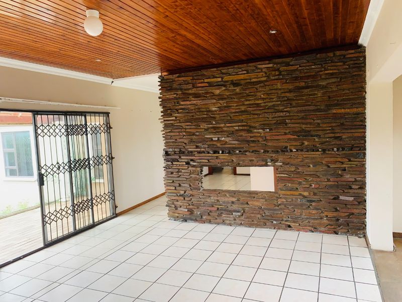 Spacious living area featuring a prominent stone fireplace wall, timber ceiling, and large sliding glass doors with security gates leading to the exterior.