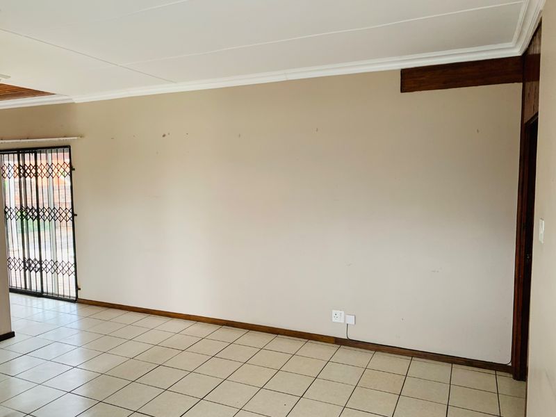 An empty living room featuring neutral walls, ceramic tiled flooring, and a sliding door with a security gate.