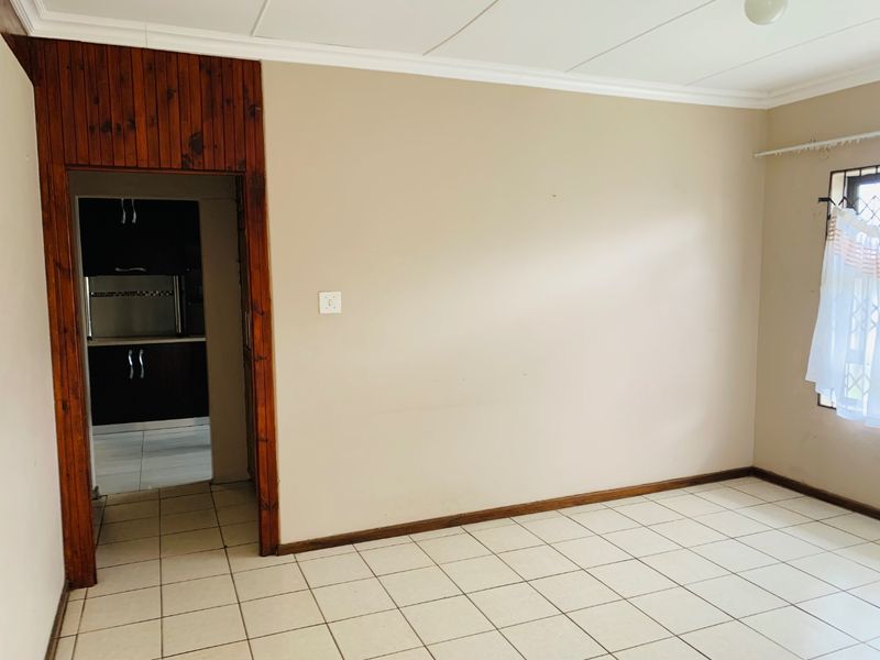 An empty living room featuring tiled flooring and a wooden doorway leading to the kitchen area.