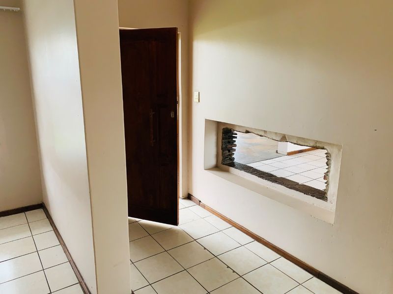 A vacant hallway featuring tiled flooring and a wooden door, with a significant unfinished wall opening requiring repair and finishing.