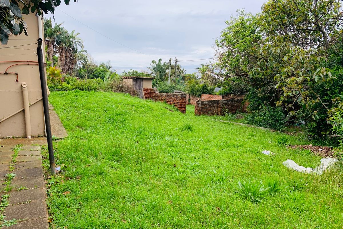 A view of the rear garden area featuring a grass lawn, concrete pathway, and brick boundary walling.