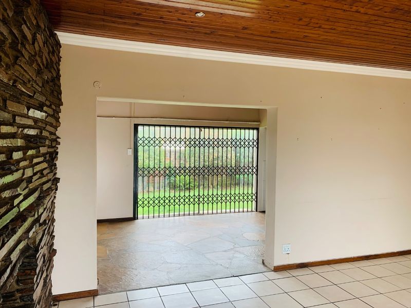 Spacious living area featuring a stone-clad feature wall, timber ceiling, and tiled flooring, with direct access to an outdoor area through a security gate.