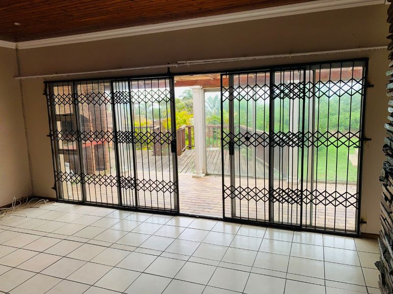 Spacious living area featuring tiled floors, a timber ceiling, and a stone feature wall, with large sliding doors opening onto an outdoor patio.