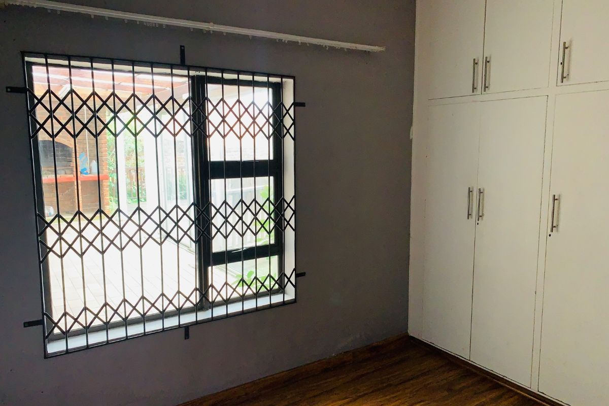 A bedroom featuring built-in cupboards, laminate flooring, and a window fitted with a security gate.
