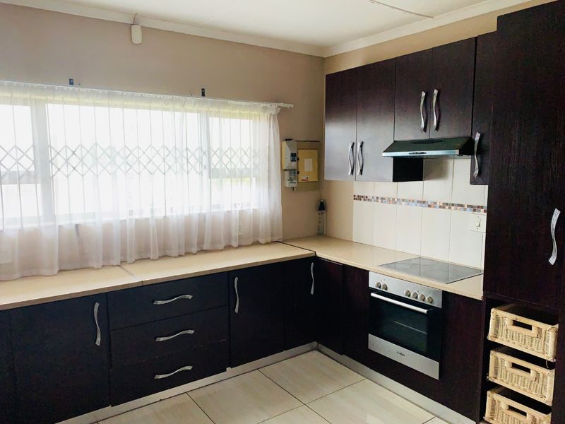 A functional kitchen featuring dark wood cabinetry, built-in oven, electric hob, extractor fan, and tiled flooring with a window security gate.