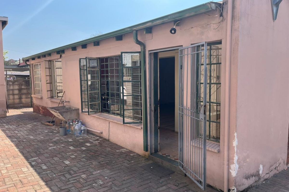 Rear exterior view of the property featuring a paved courtyard, steel-framed windows, and a security gate entrance.