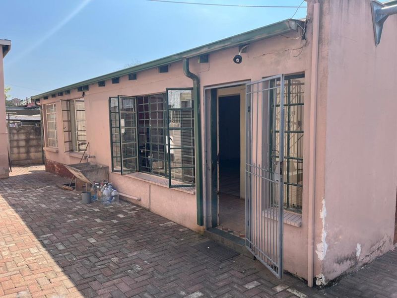 Rear exterior view of the property featuring a paved courtyard, steel-framed windows, and a security gate entrance.
