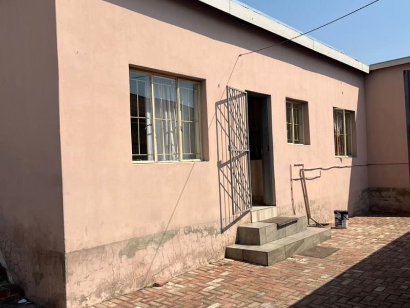 Rear exterior view of the property featuring a paved courtyard, security gate, and tiled entrance steps with visible wear to the exterior wall finish.