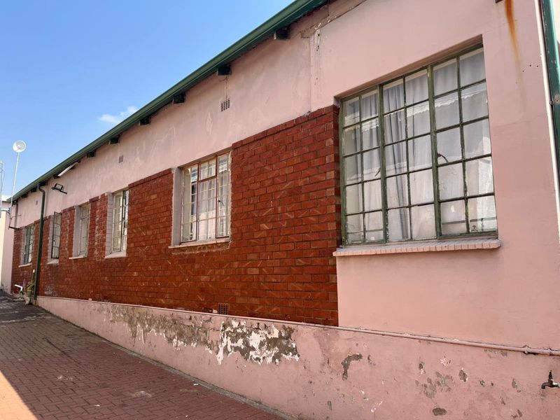 Exterior view of the building side featuring steel-framed windows, brick detailing, and a paved walkway, showing signs of significant wear and peeling exterior paint.
