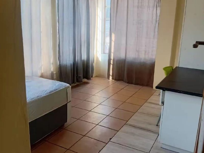 A bedroom featuring tiled flooring, built-in cabinetry, and large windows with curtain rods, offering a functional space with potential for cosmetic updates.