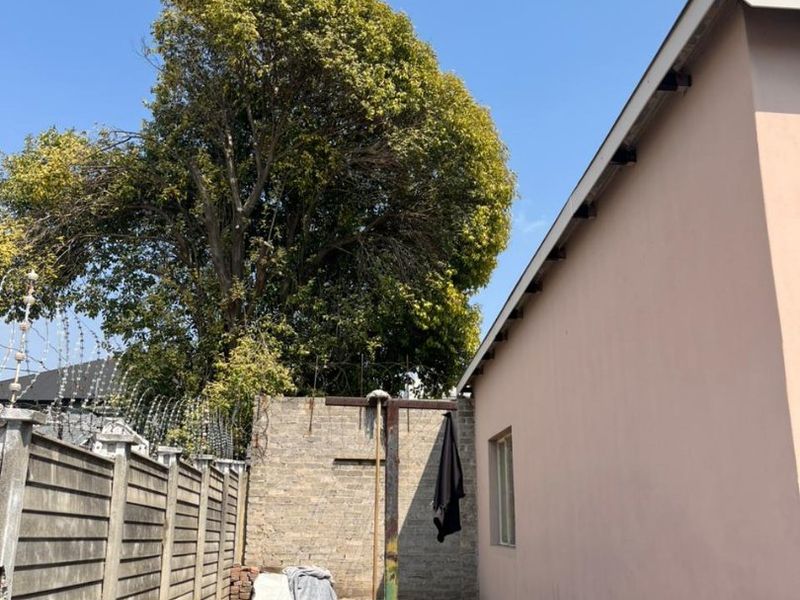 A rear exterior area featuring a concrete paved yard, boundary wall with security razor wire, and a metal washing line pole.