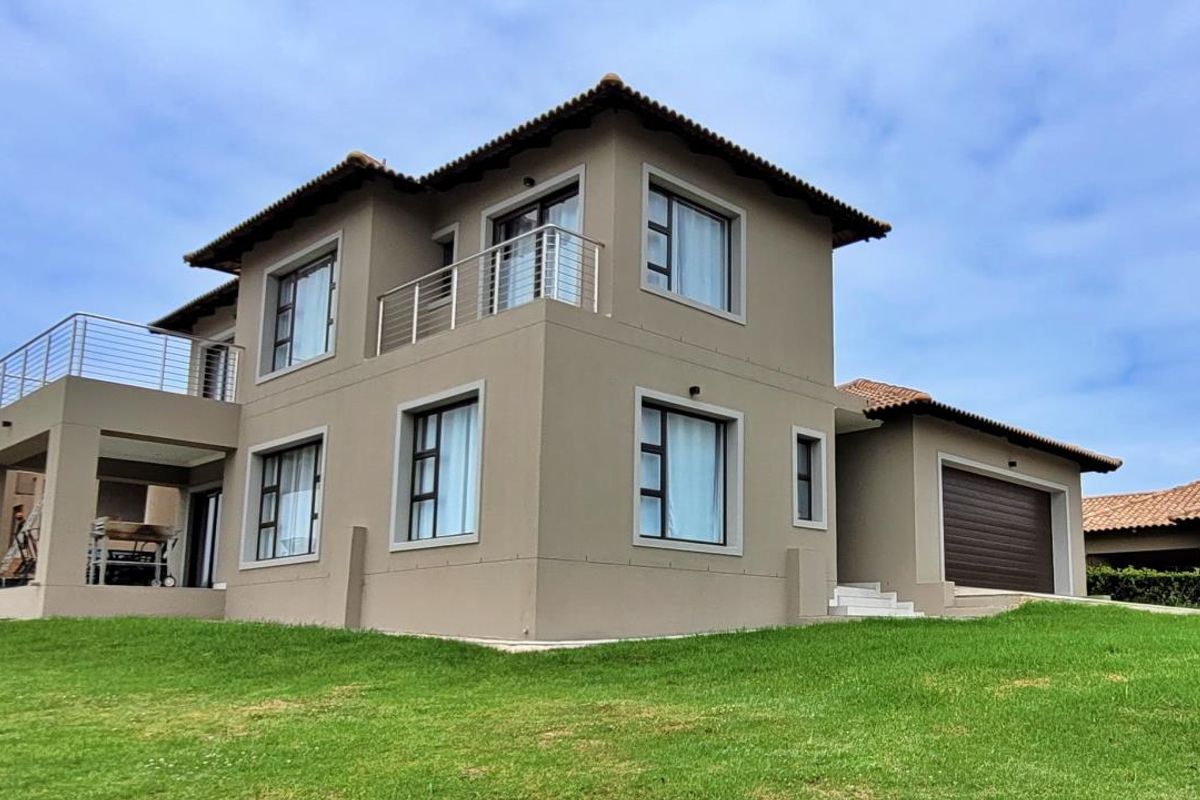A modern double-story residential home featuring a tiled roof, balcony with stainless steel railings, covered patio, and an integrated double garage.