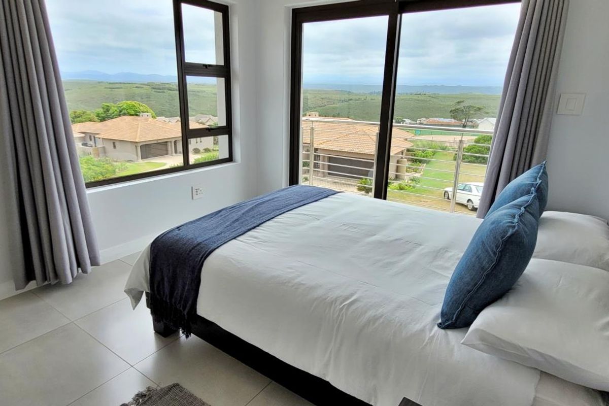 A bright bedroom featuring large windows and a sliding glass door that opens to a balcony with scenic views.
