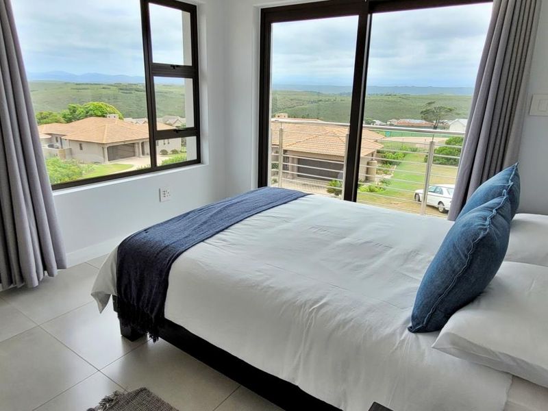 A bright bedroom featuring large windows and a sliding glass door that opens to a balcony with scenic views.
