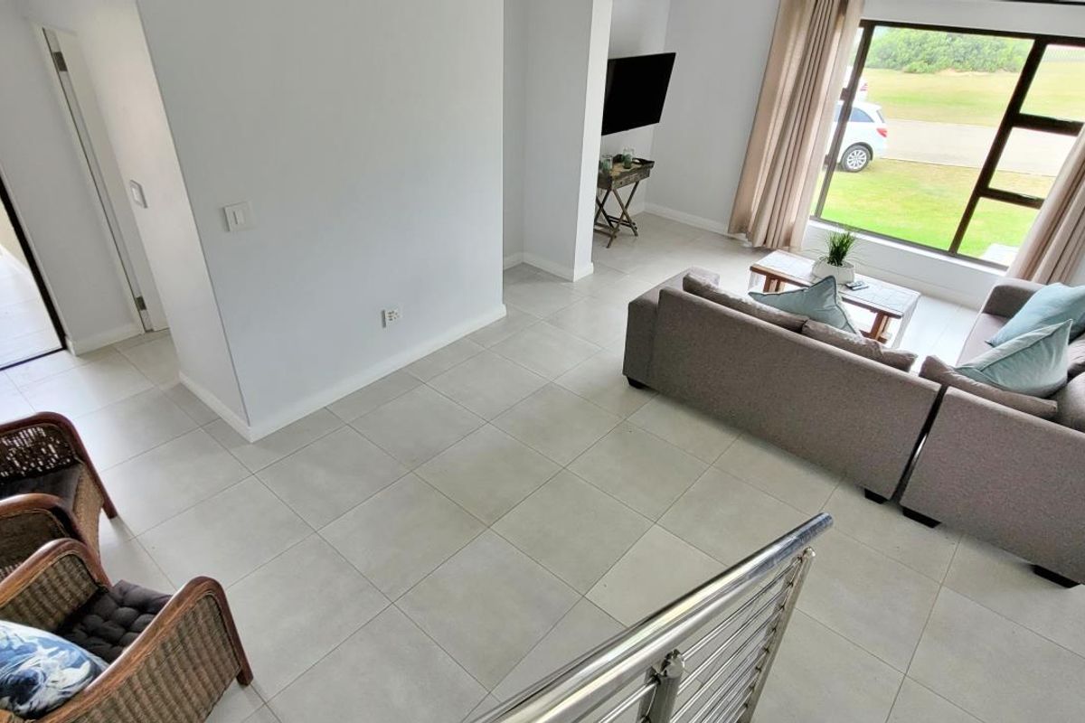 A bright, open-plan living area featuring large windows, tiled flooring, and a modern stainless steel balustrade, with direct access to an outdoor patio.