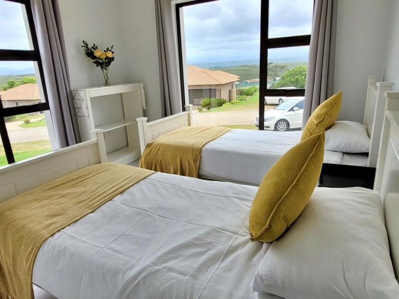 A bright bedroom featuring large aluminium-framed windows that provide ample natural light and views of the surrounding estate.