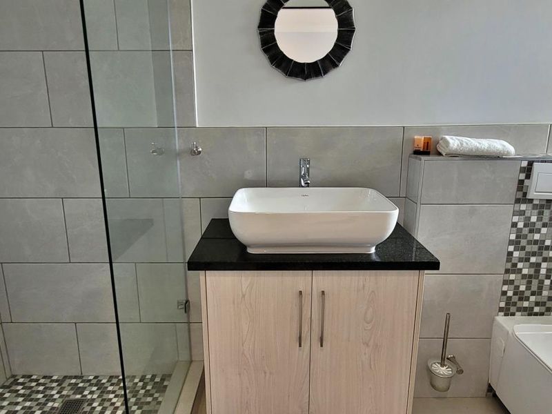 Modern bathroom featuring a vessel sink on a granite vanity, glass-enclosed shower, and wall-mounted toilet with stylish mosaic tile detailing.