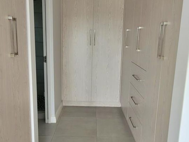 A clean, modern walk-in dressing area or hallway featuring extensive built-in cabinetry with light wood-grain finish and neutral floor tiles.