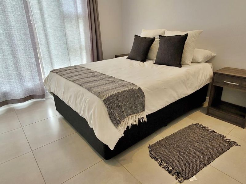 A well-maintained bedroom featuring neutral tiled flooring and a large sliding glass door that provides natural light.