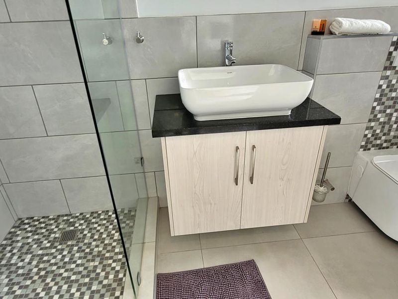 Modern bathroom featuring a vessel sink on a granite vanity, wall-hung toilet, and a glass-enclosed shower with mosaic tile detailing.