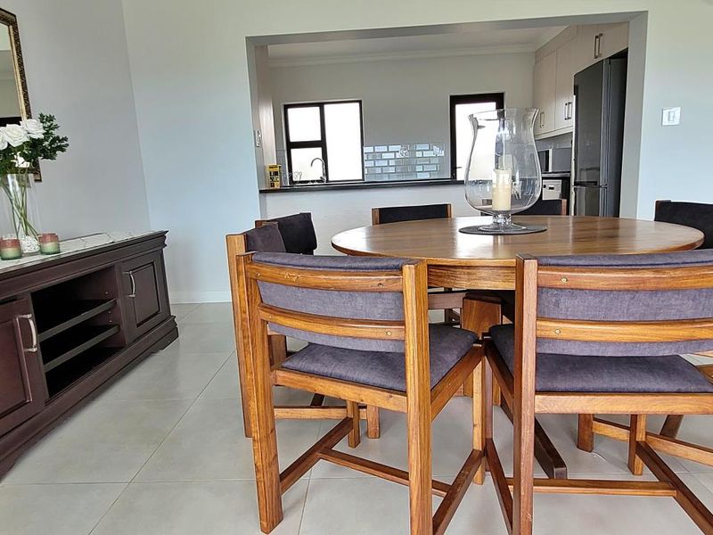 Open plan dining area flowing into a functional kitchen with modern cabinetry, subway tile backsplash, and neutral tiled flooring throughout.
