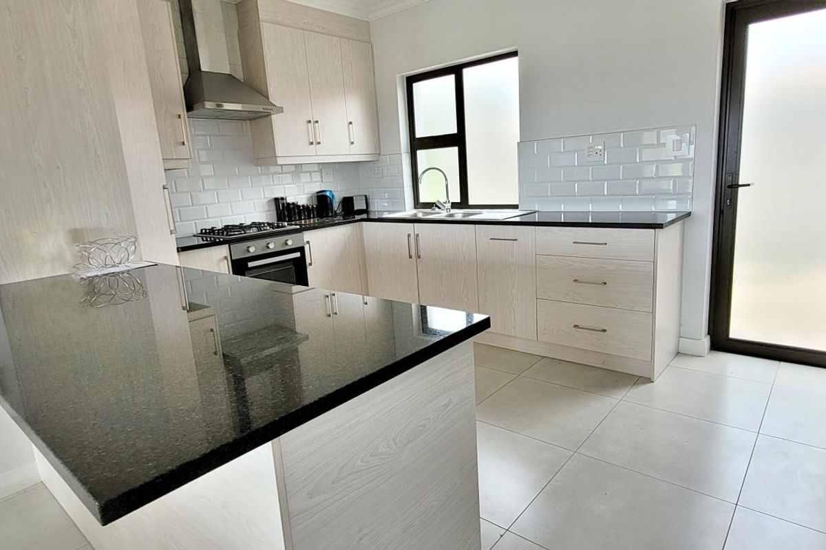 Modern kitchen featuring light wood cabinetry, granite countertops, subway tile backsplash, and integrated stainless steel appliances with direct access to the exterior.
