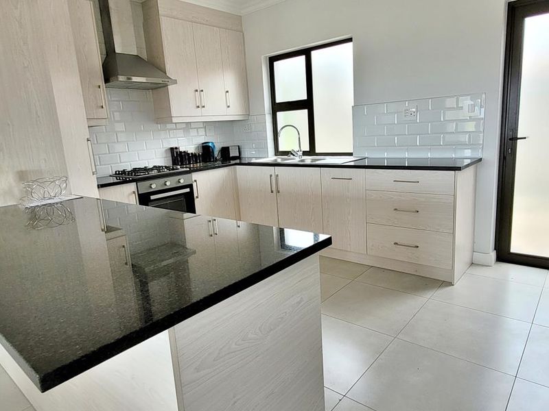 Modern kitchen featuring light wood cabinetry, granite countertops, subway tile backsplash, and integrated stainless steel appliances with direct access to the exterior.