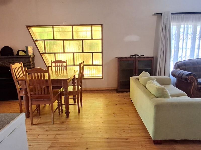 Spacious open-plan living and dining area featuring warm timber flooring, a unique feature glass block window, and a built-in fireplace.