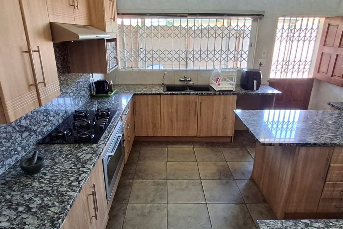 A functional kitchen featuring granite countertops, wooden cabinetry, a built-in oven with gas hob, and tiled flooring with direct access to the exterior.