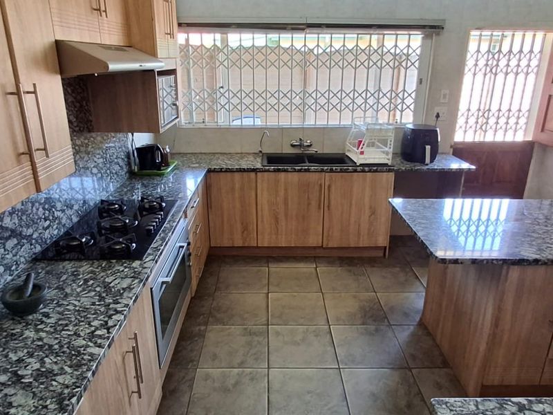 A functional kitchen featuring granite countertops, wooden cabinetry, a built-in oven with gas hob, and tiled flooring with direct access to the exterior.