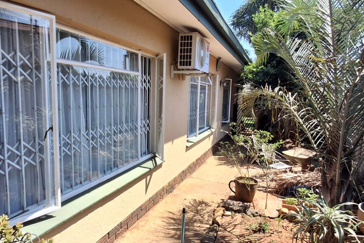 Rear exterior view of the house featuring plastered walls, security gates on windows, and an external air conditioning unit.