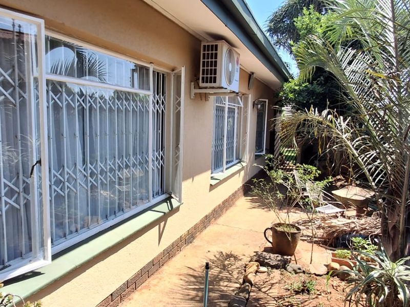Rear exterior view of the house featuring plastered walls, security gates on windows, and an external air conditioning unit.