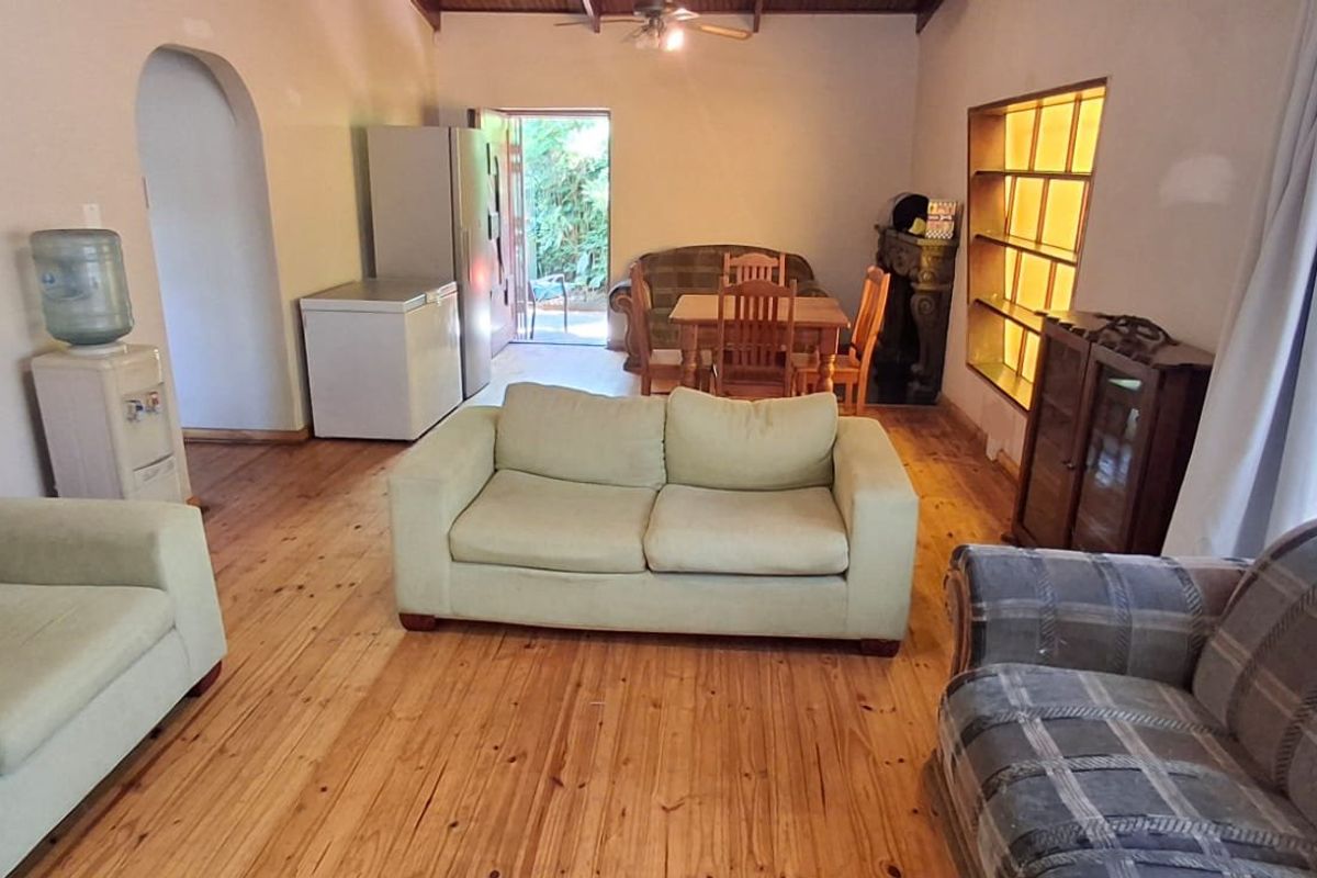 Spacious living area featuring warm timber flooring, exposed beam ceiling, and an arched doorway leading to adjacent spaces.