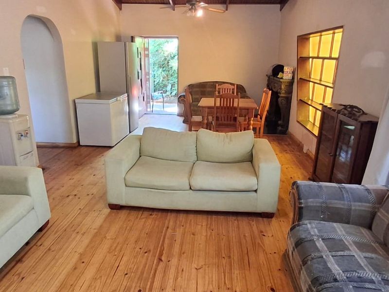 Spacious living area featuring warm timber flooring, exposed beam ceiling, and an arched doorway leading to adjacent spaces.