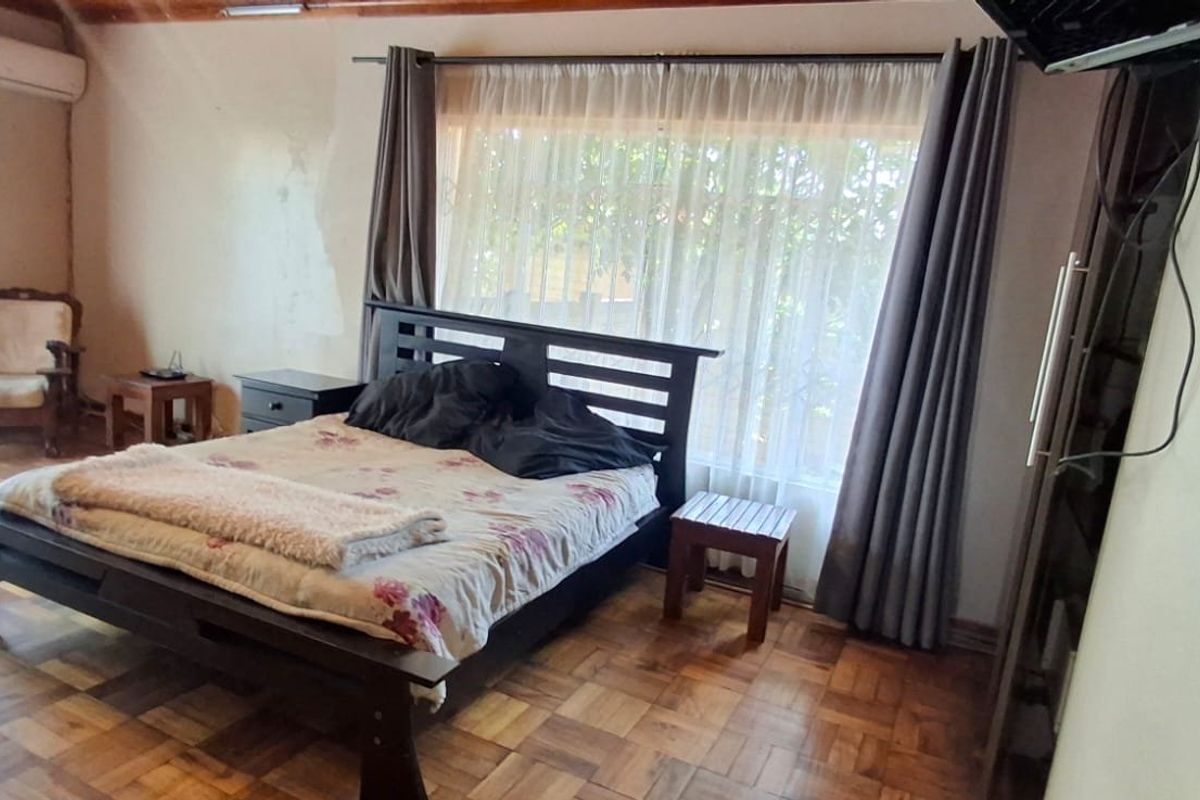 Spacious bedroom featuring classic parquet flooring, exposed timber ceiling beams, and a wall-mounted air conditioning unit.