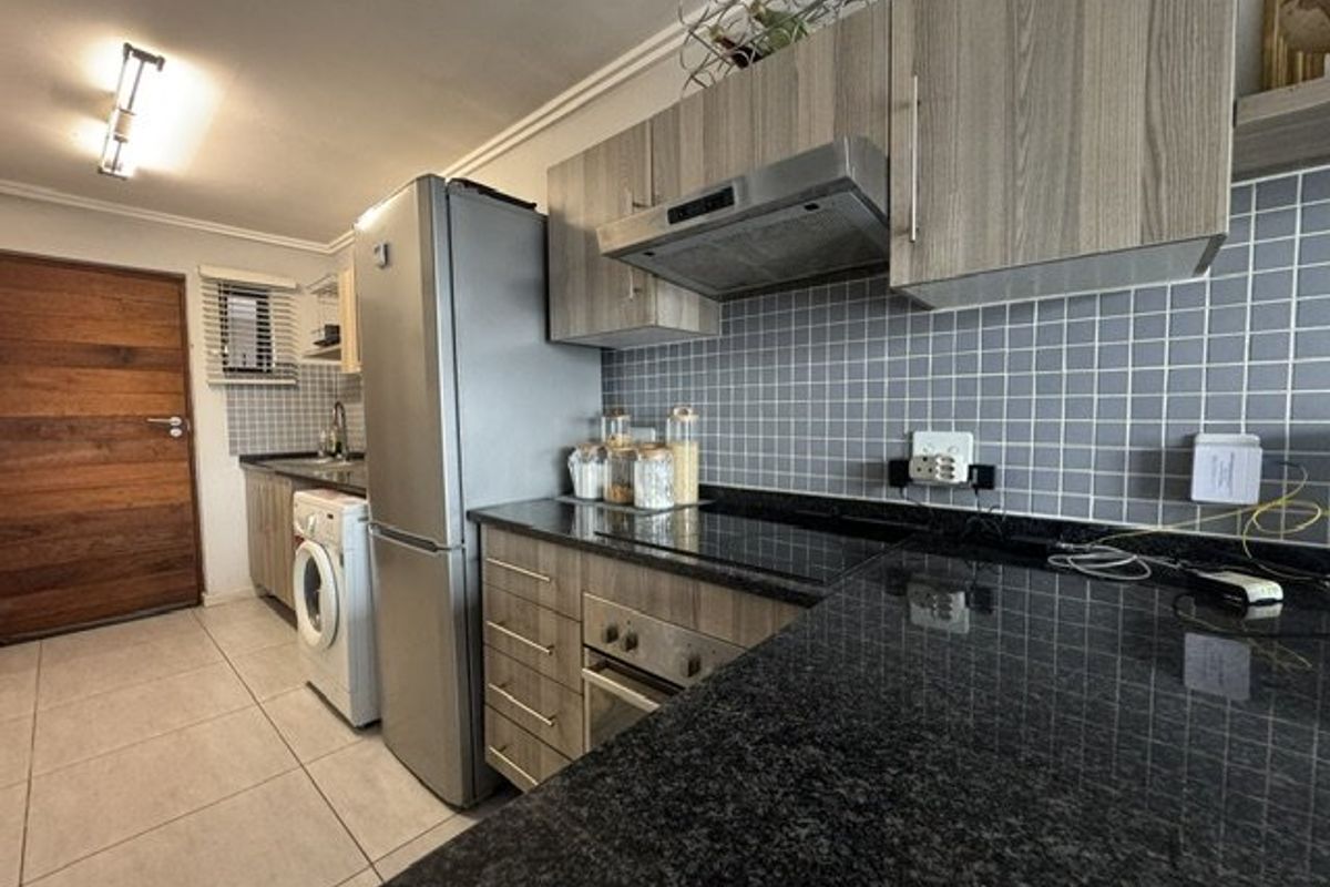 A functional kitchen featuring granite countertops, built-in cabinetry, a hob, oven, and extractor fan, with tiled flooring and a tiled backsplash.