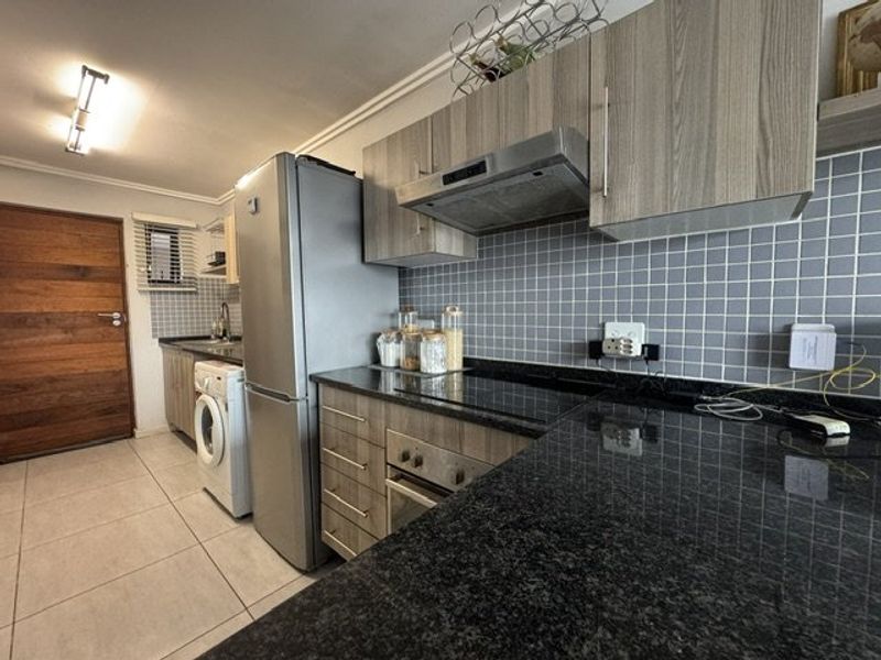 A functional kitchen featuring granite countertops, built-in cabinetry, a hob, oven, and extractor fan, with tiled flooring and a tiled backsplash.