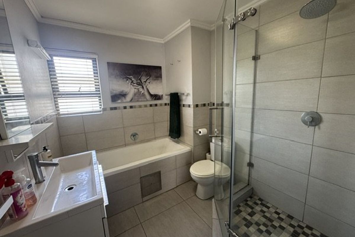 Modern bathroom featuring a glass-enclosed shower with rain head, a built-in bathtub, vanity basin, and neutral tiled finishes throughout.