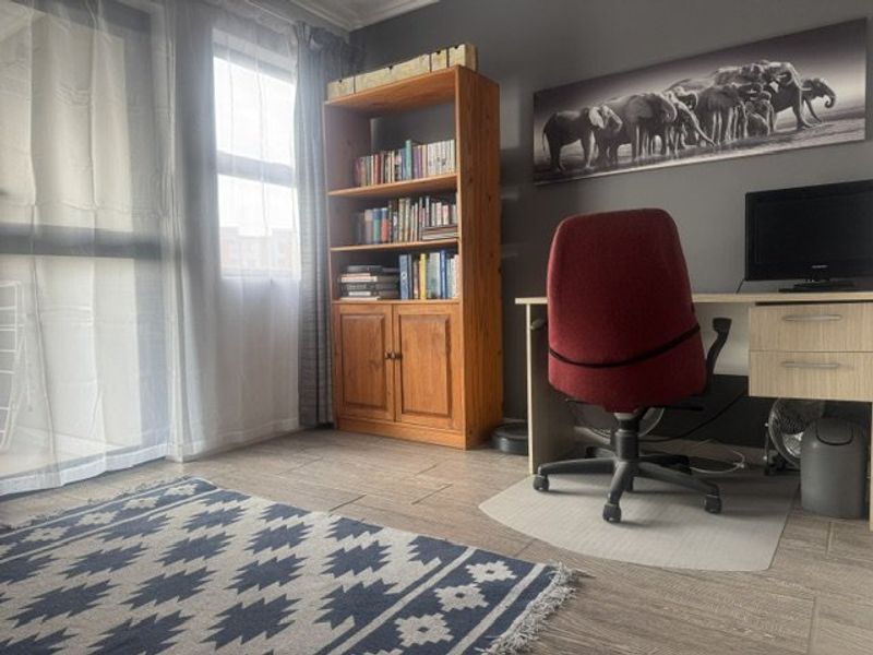 A functional home office space featuring tiled flooring and natural light from a large window, providing a quiet area for work or study.