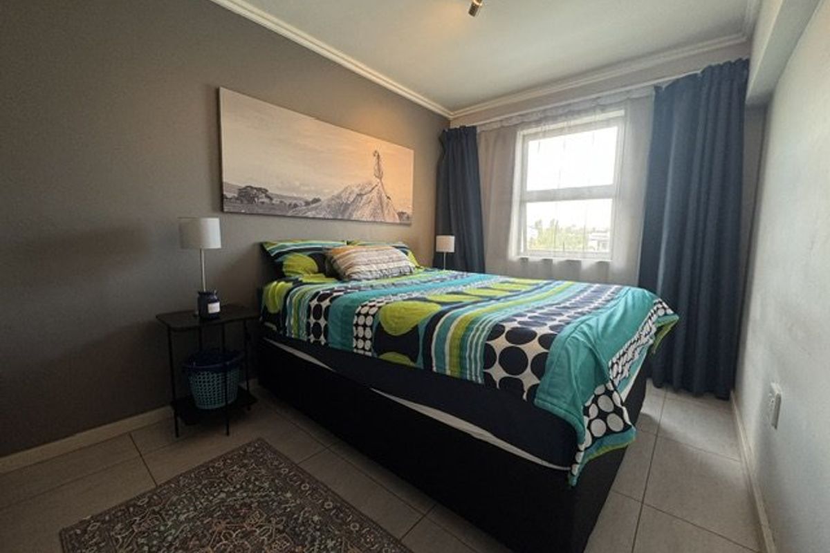 A bedroom featuring tiled flooring, ceiling cornice, and a window with curtains, providing a functional and neutral living space.