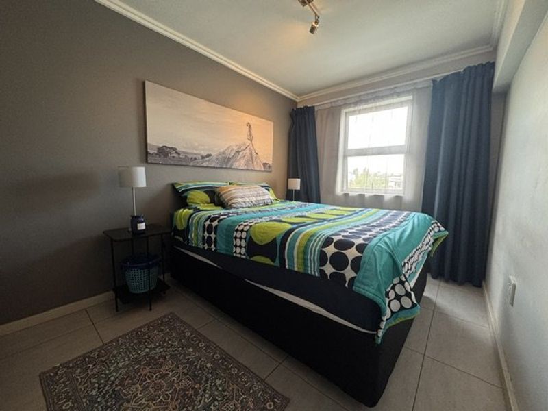 A bedroom featuring tiled flooring, ceiling cornice, and a window with curtains, providing a functional and neutral living space.