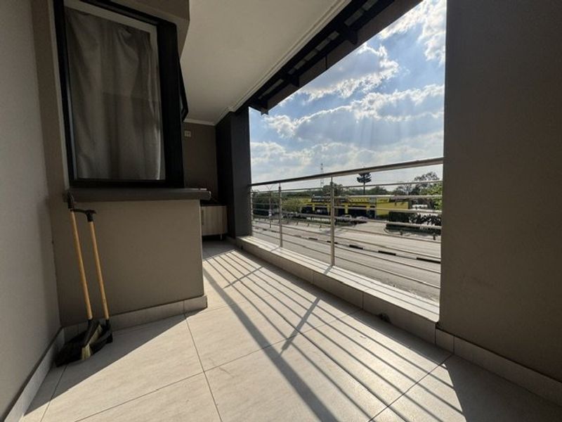 A spacious covered balcony featuring tiled flooring and a modern stainless steel balustrade, offering an open view of the surrounding area.